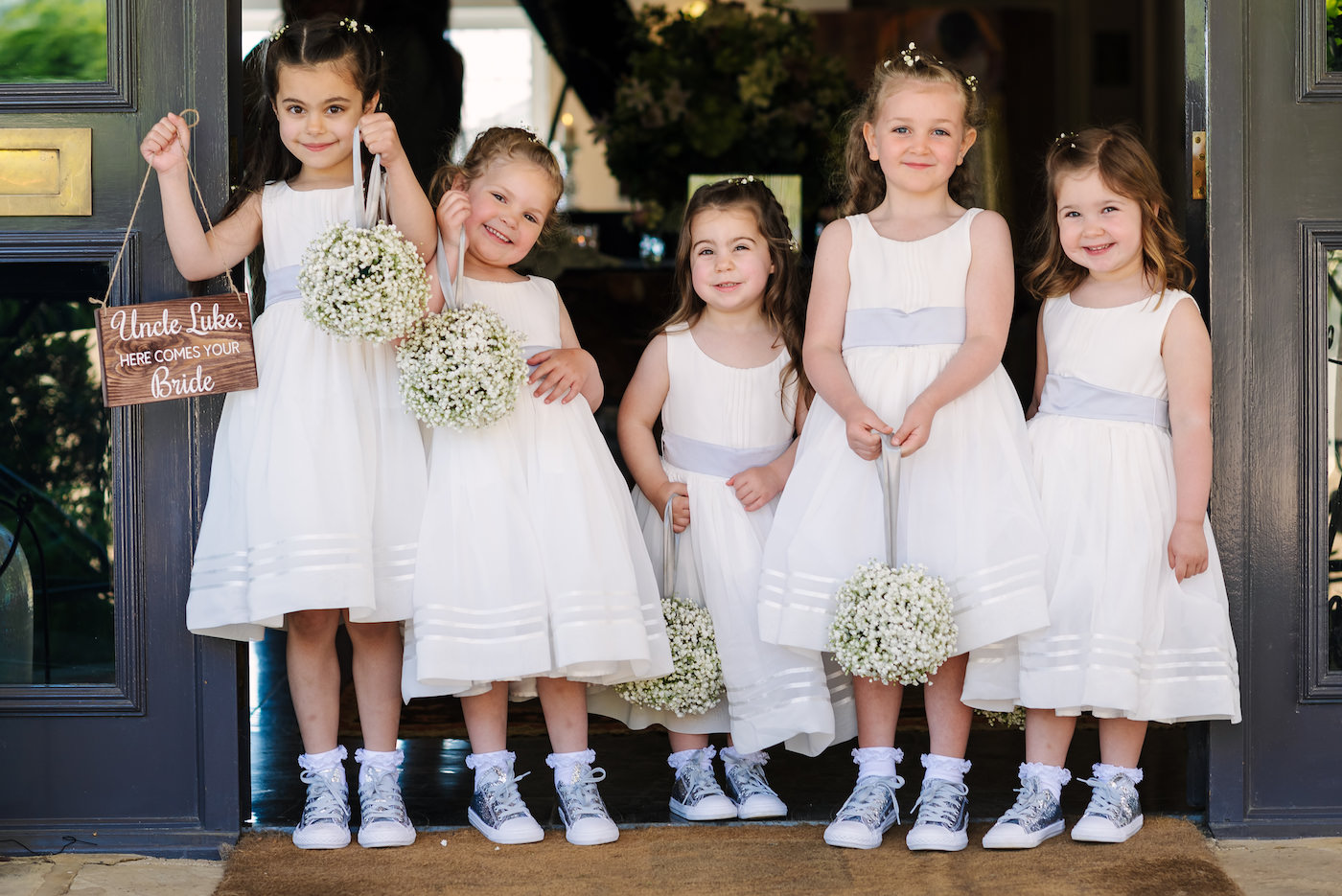 Five flower girls in white dresses holding white baby breath gypsophila pomanders