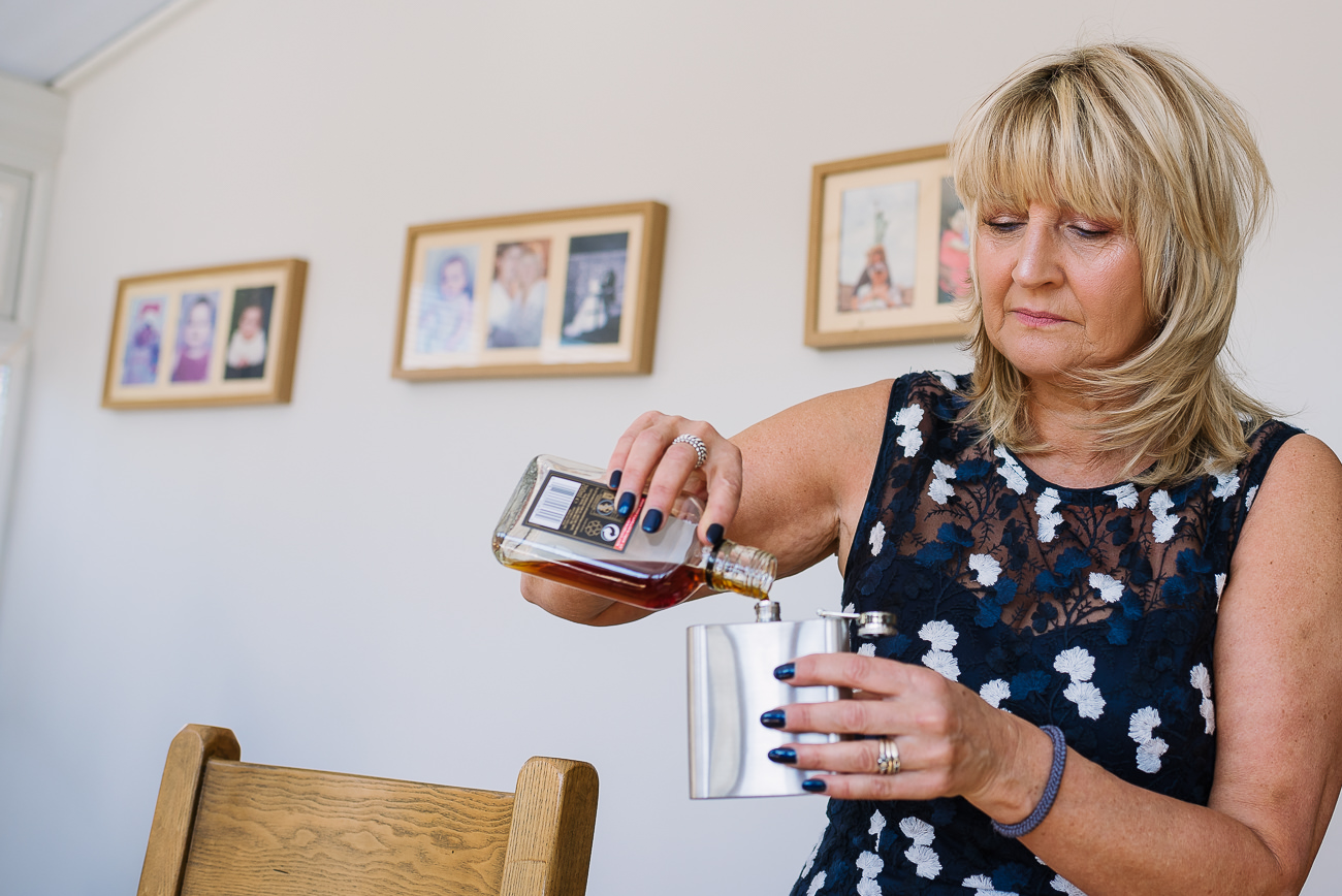 Mother of the groom filling a hip flask with alcohol