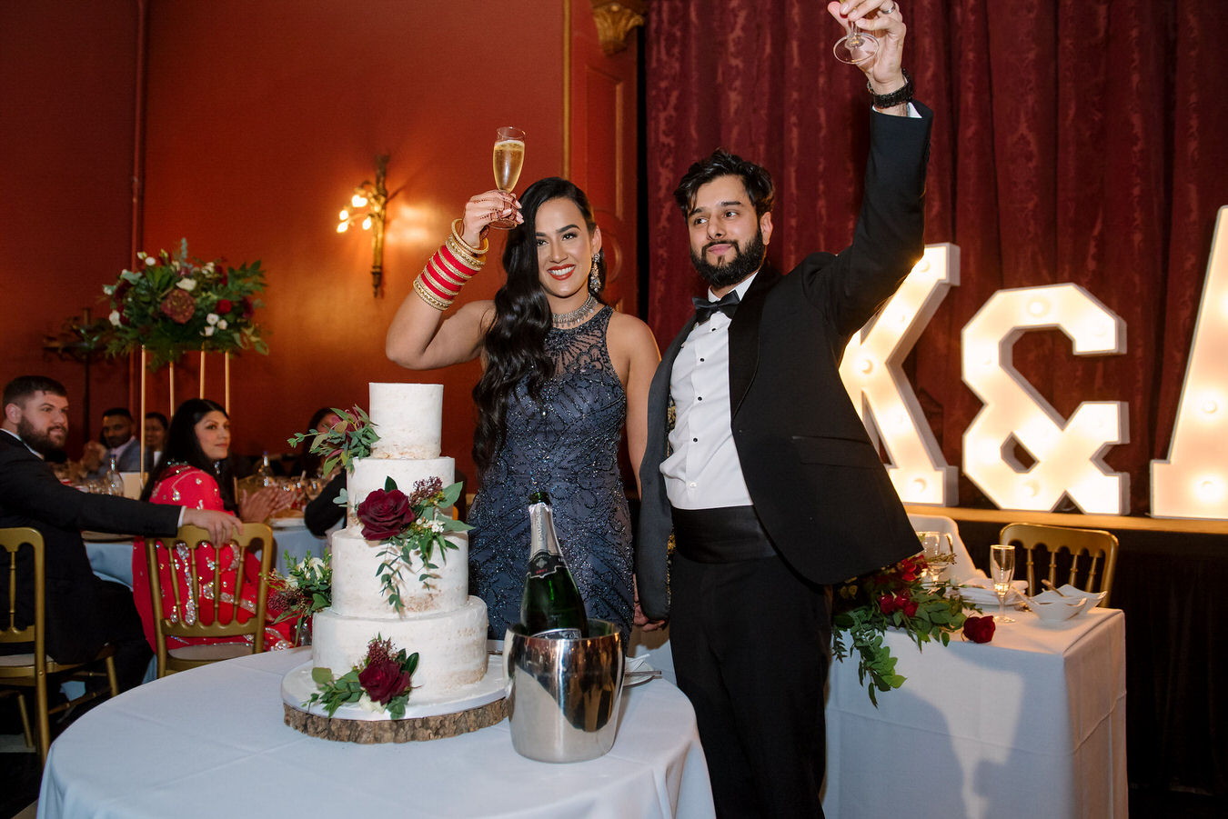 Bride and groom are lifting the glasses up cheering after cutting their wedding cake.