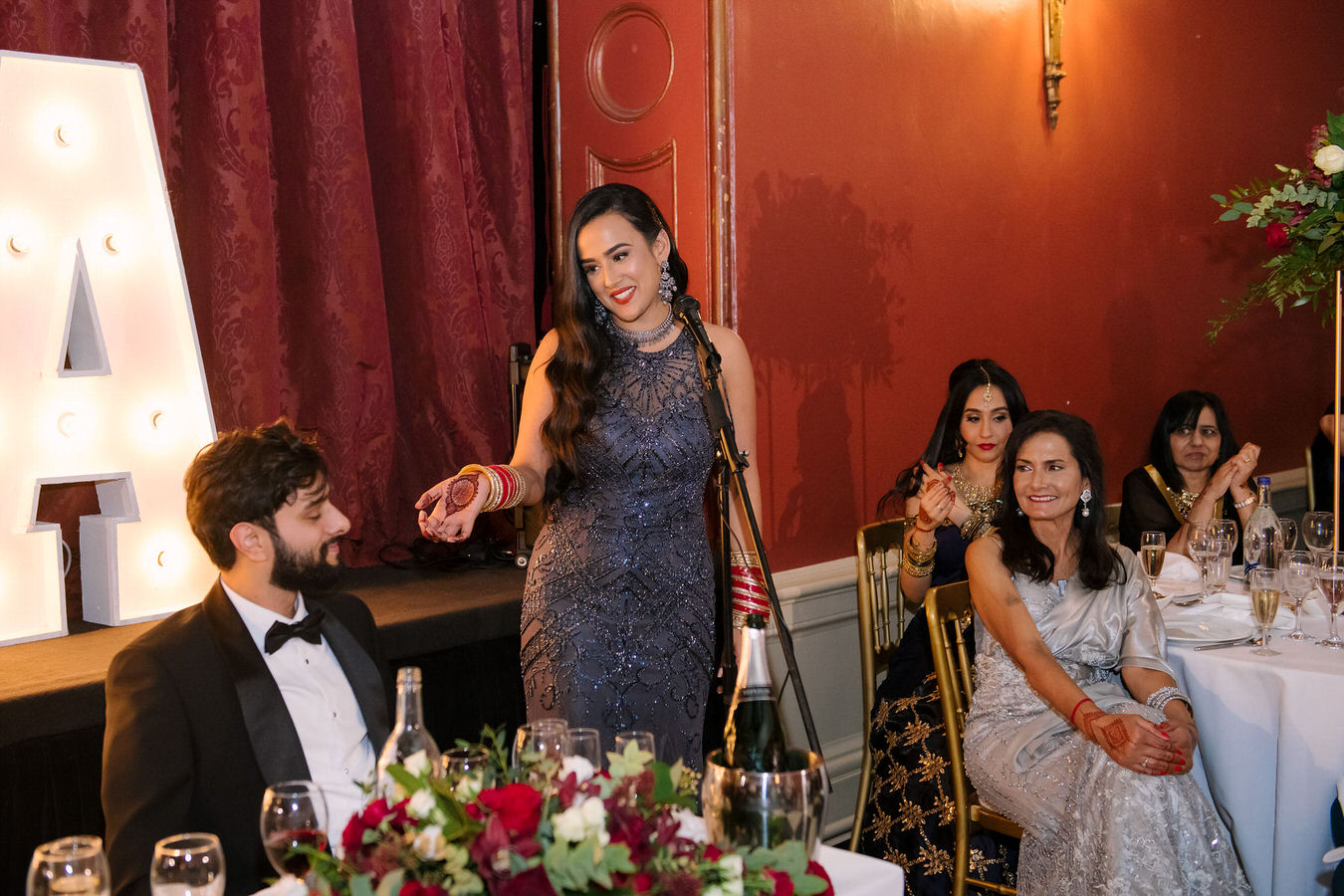 Sikh wedding photography bride is having a speech about the groom showing with her hand towards him at Hampton Court House