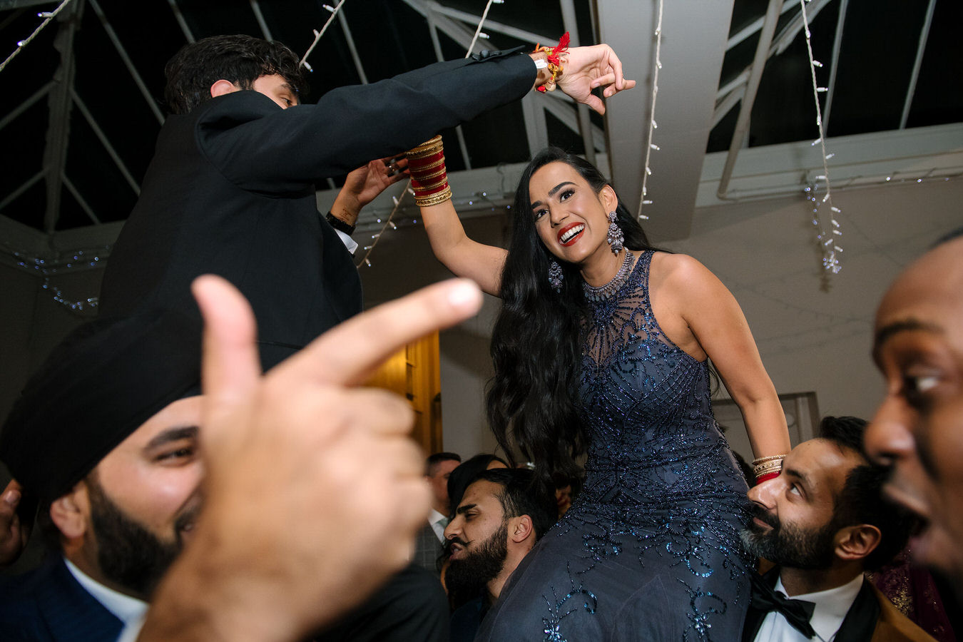 Asian couple dancing on guest’s shoulders during London wedding reception at Hampton Court House.