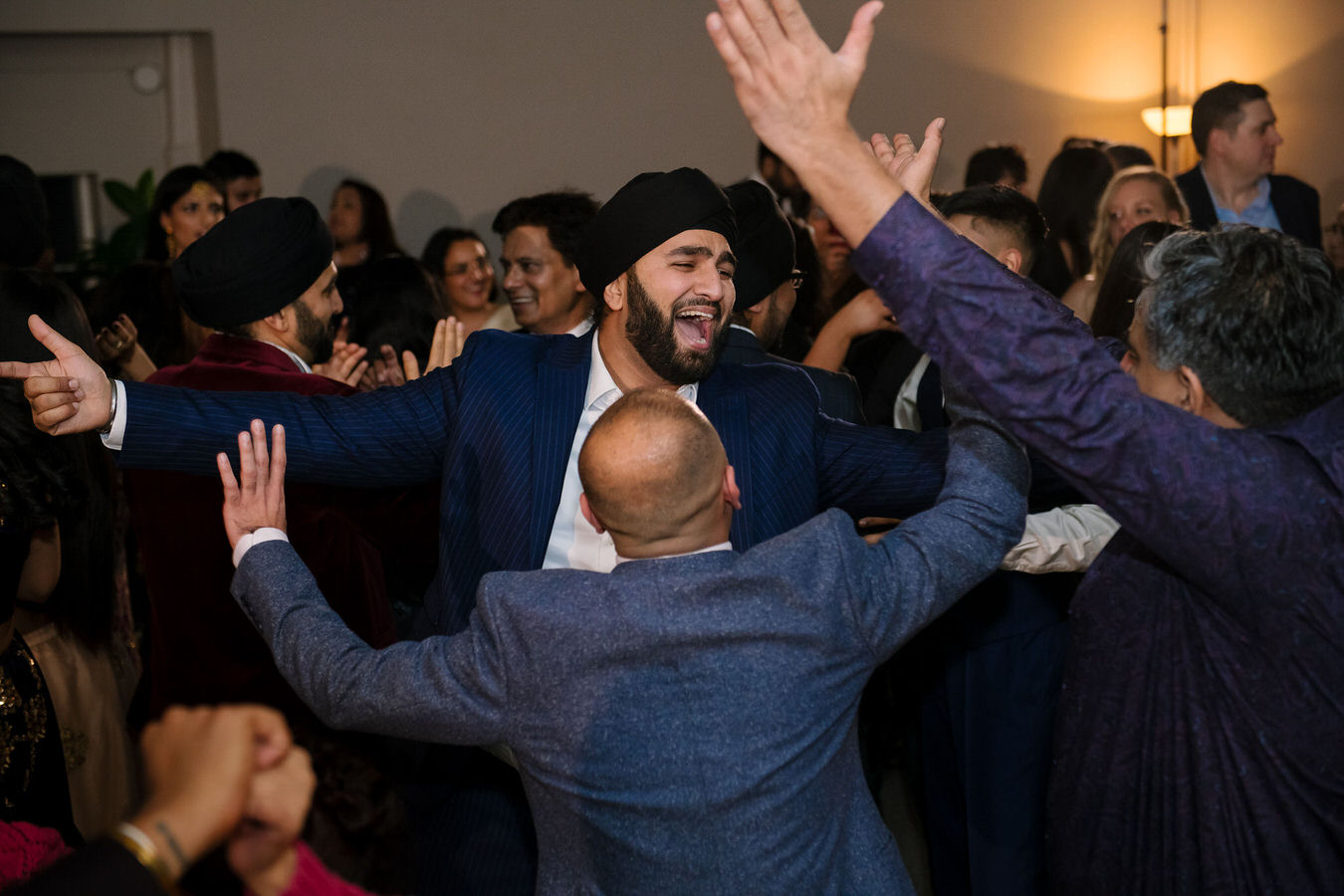 Sikh Asian wedding man’s are singing Indian songs with their arms up in the air.