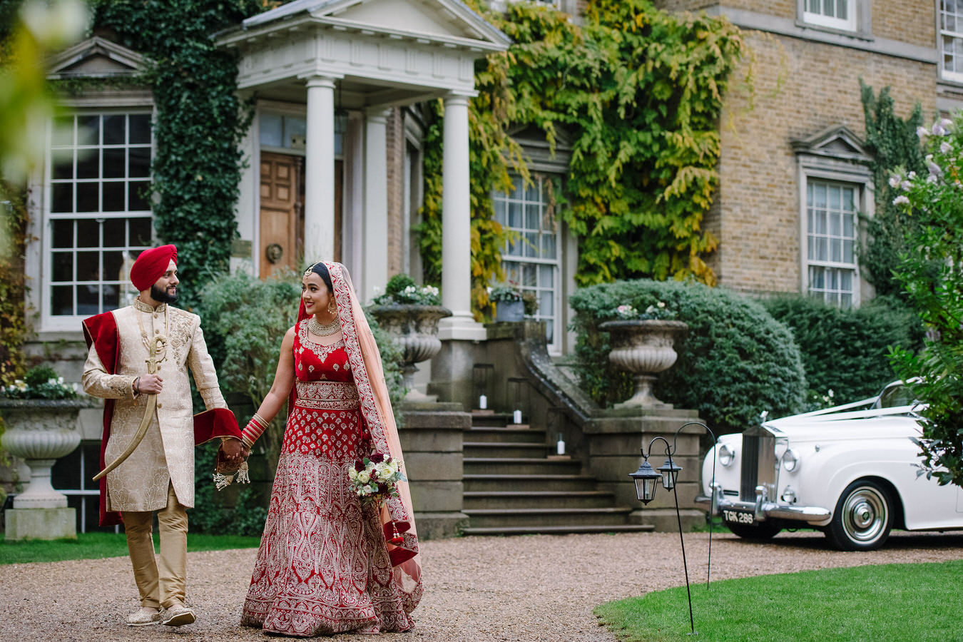 Bride dressed in a bridal lehenga and groom in a Punjabi outfit with kirpan walking hand in hand during their Sikh wedding at Hampton Court House