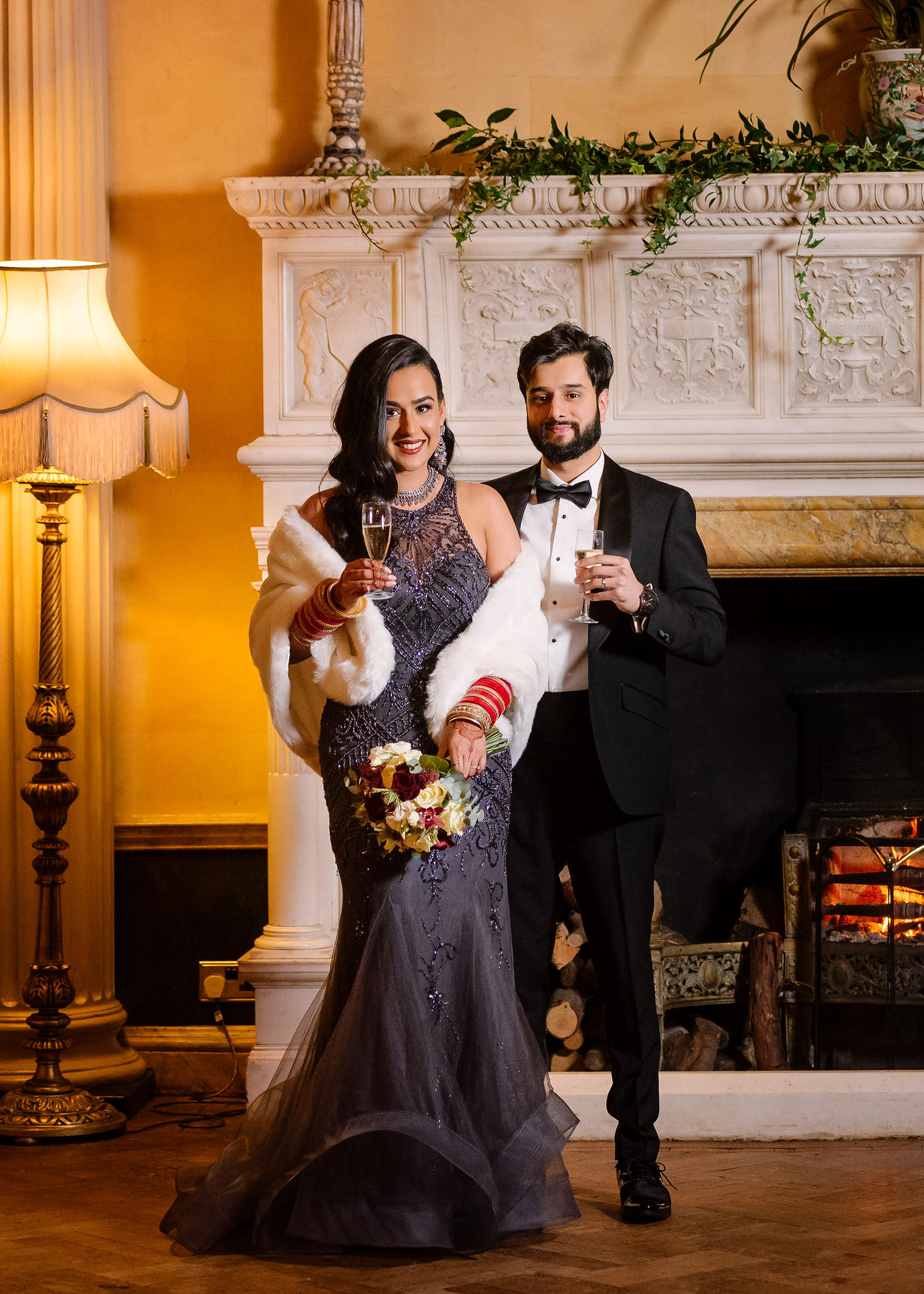 Asian wedding bride and groom with champagne glasses standing in front of the fireplace