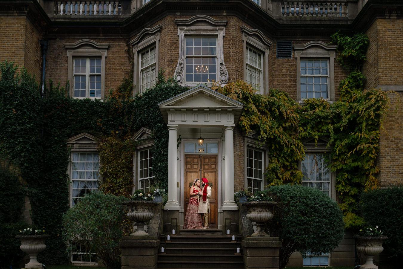 Asian wedding photography of bride and groom on the entrance stairs at Hampton Court holding hands and looking at each other.