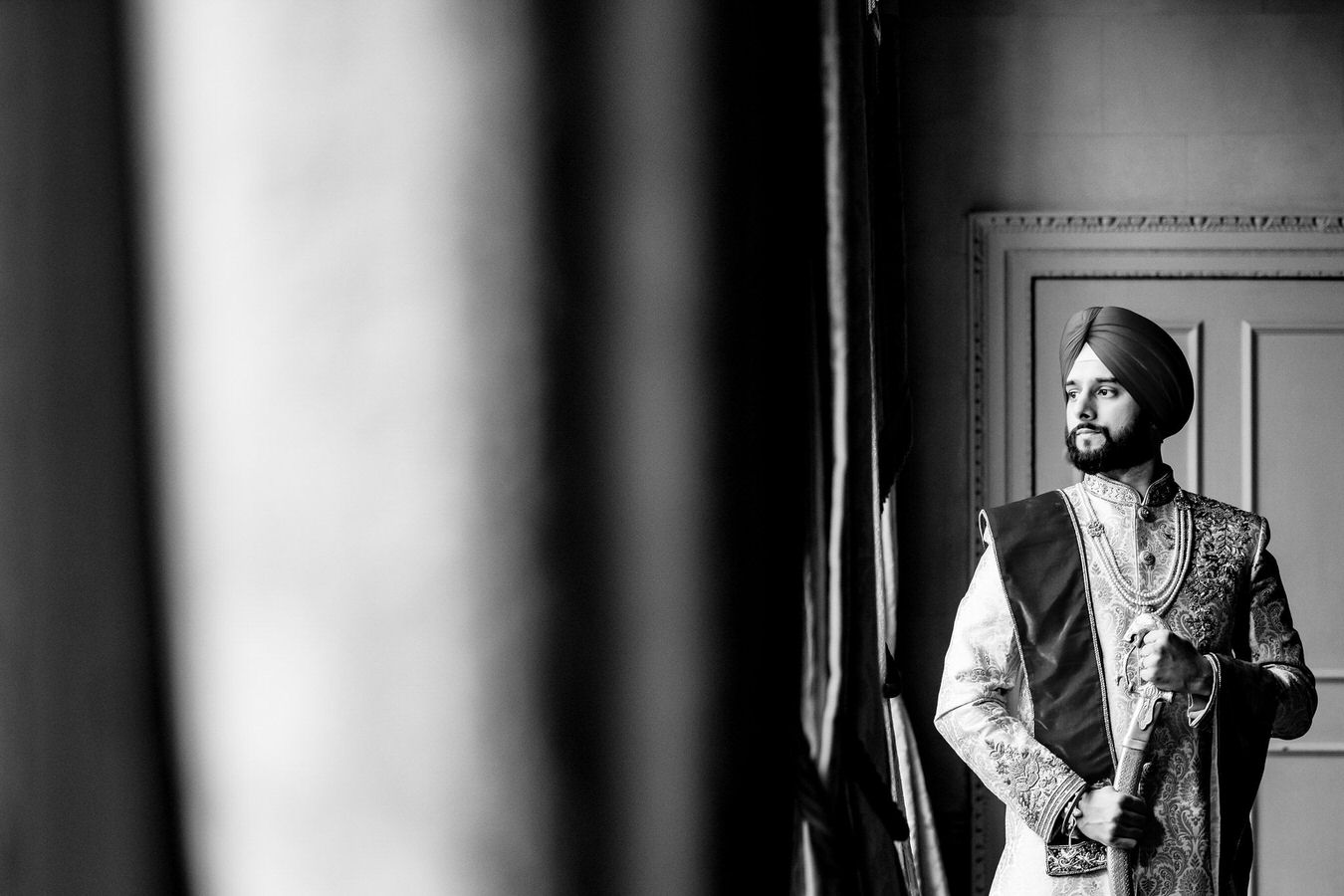 Sikh wedding black and white photography of a groom with kirpan in his hands and a turban looking at his right.
