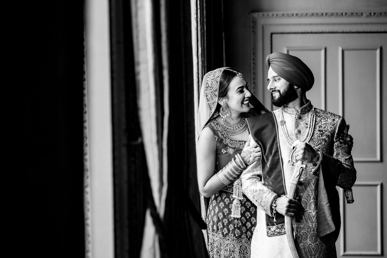 Black and white photo with Asian bride and groom side by side looking in each other's eyes.