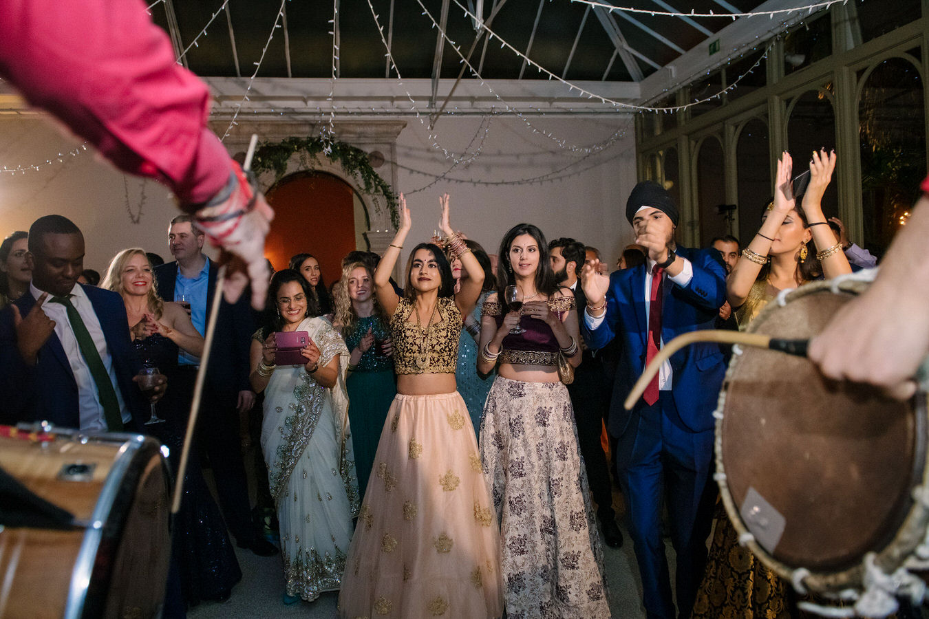 Wedding guests are dancing and clapping their hands as the dhol drummers beat the drums.