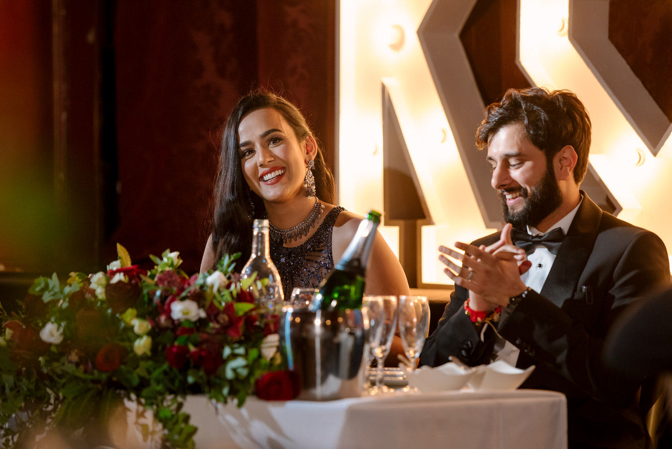 Groom is clapping and the bride is smiling at their sweetheart table at Hampton Court House.