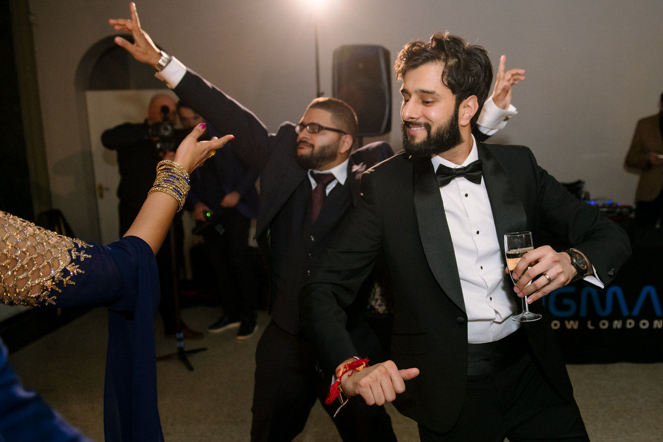 Groom dressed in a black tuxedo is dancing with a glass in his hand and feeling great at Hampton Court House.