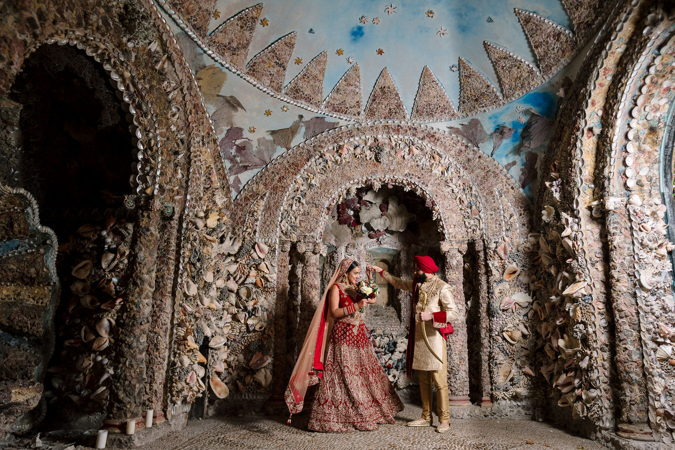 Sikh Asian wedding groom with his kirpan in hand and a bride with a bouquet are dancing inside the shell grotto