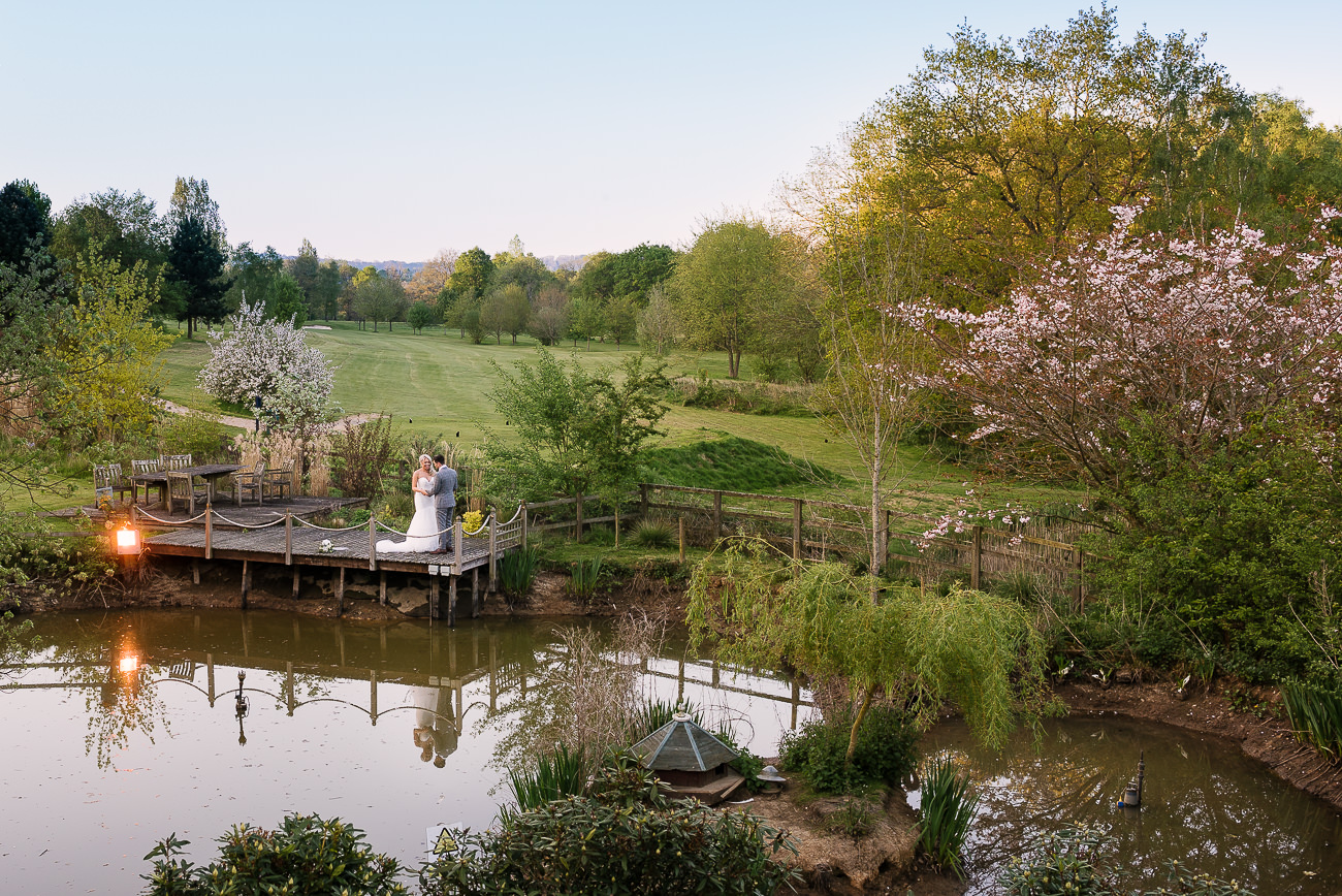 Wide photograph of the bride and groom standing by the Russets pond at sunset overlooking the grounds at Russets