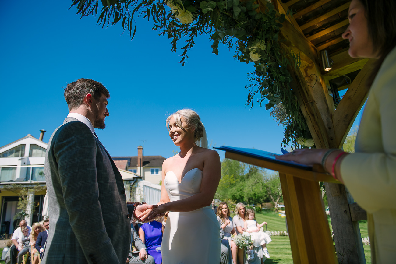 Groom and bride are smiling to each other during outdoor ceremony