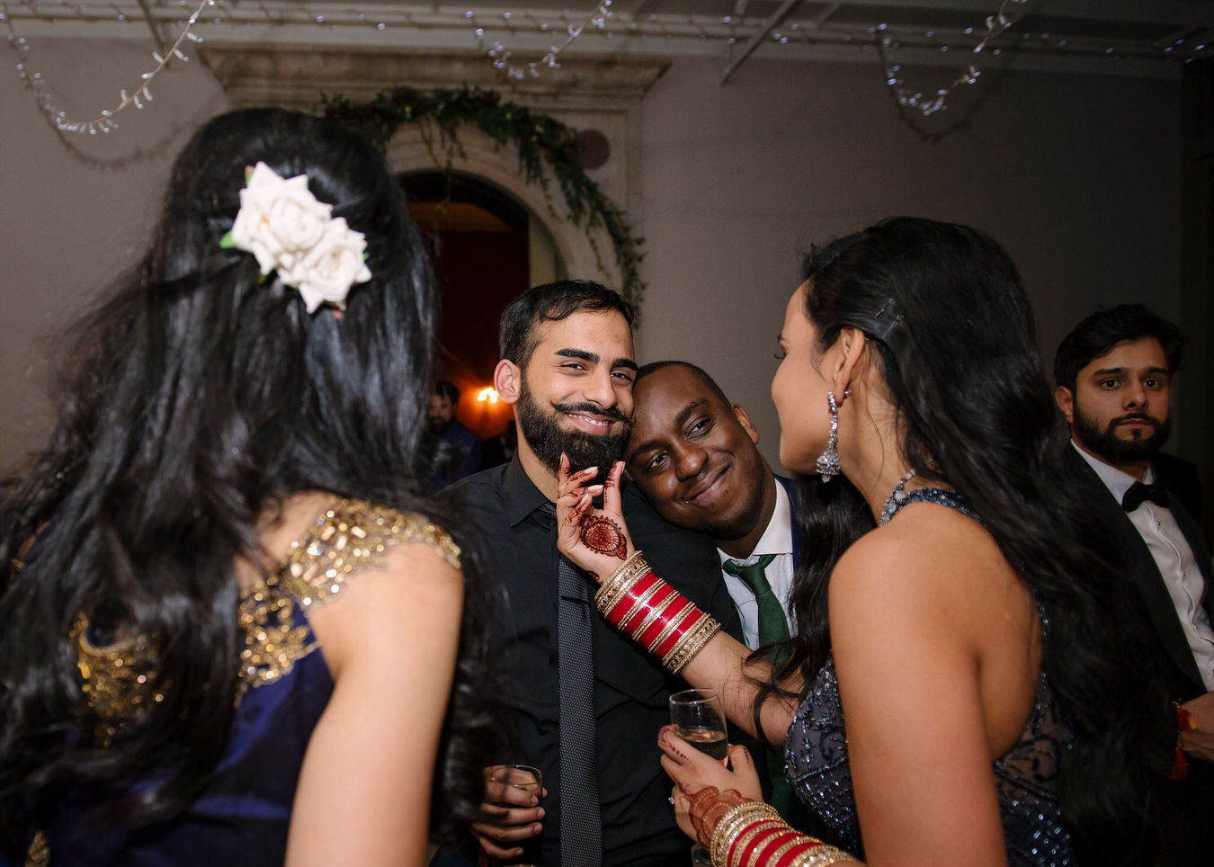 Documentary Asian wedding photographer captures a moment between the bride and one of her friends, the bride is touching her friend’s beard.