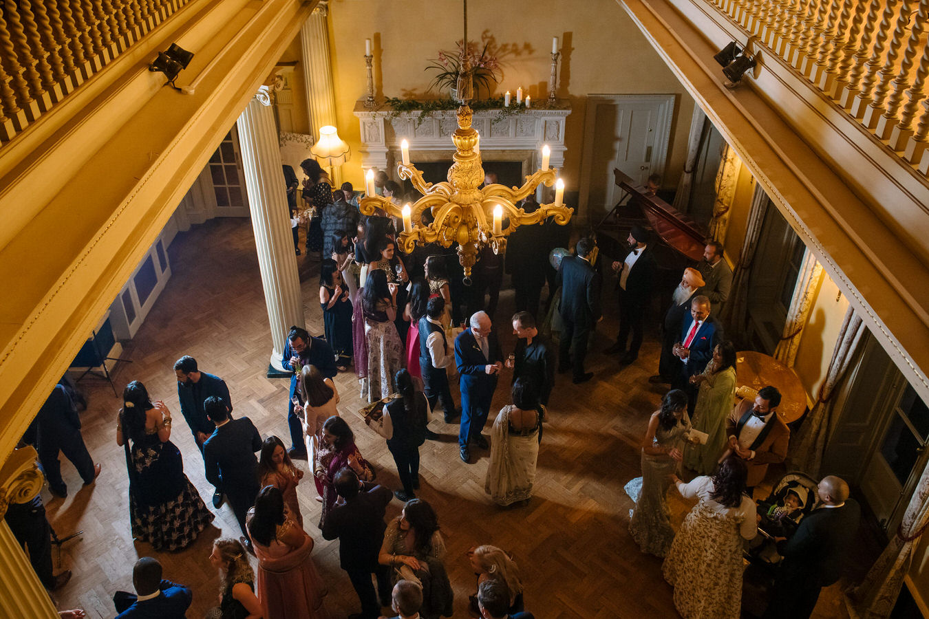 Photo taken from the first floor looking down to wedding guests chatting and feeling good during wedding reception at Hampton Court House.