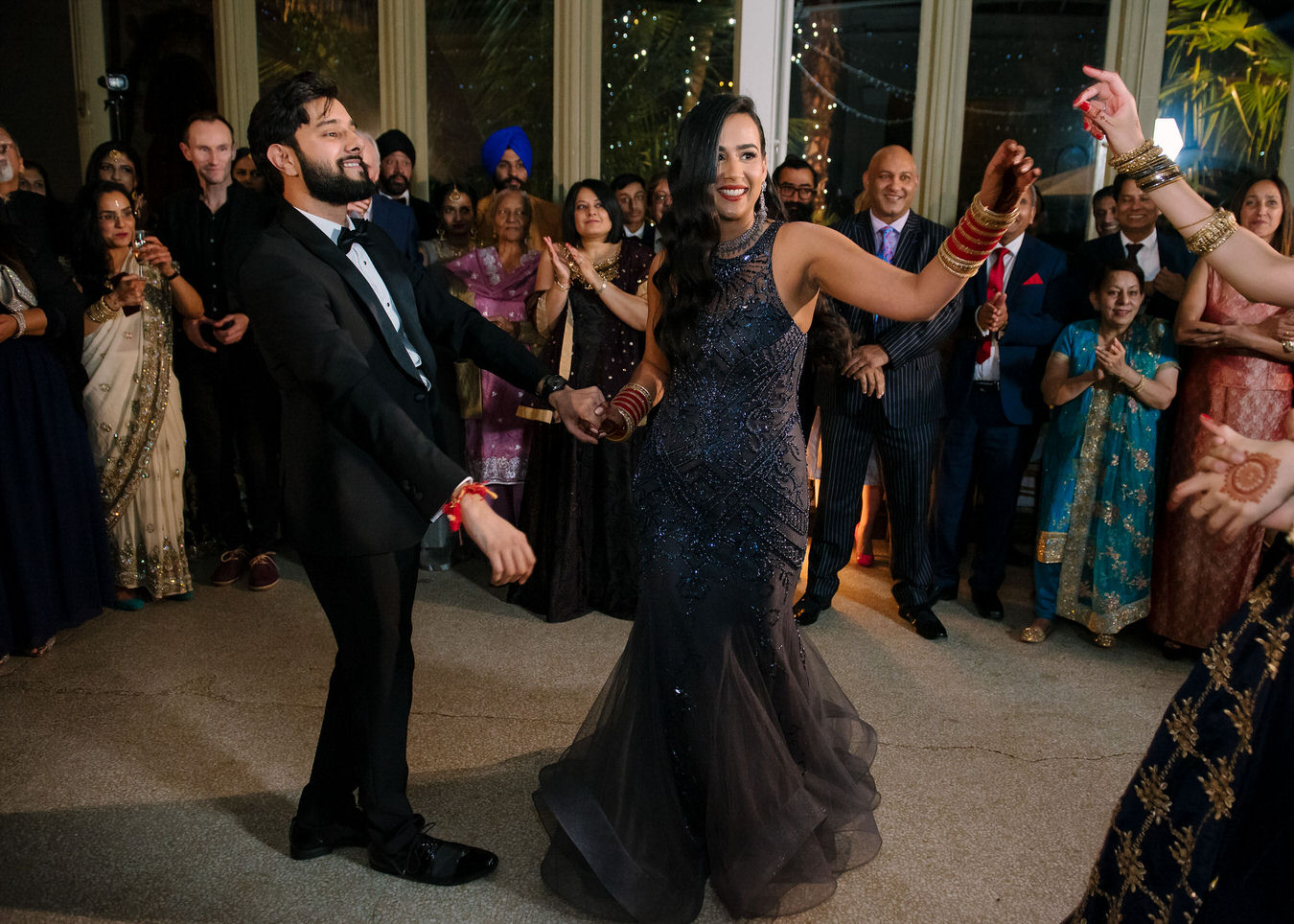 Bride and groom Sikh wedding are dancing together in the center of the room and the guests applaud them