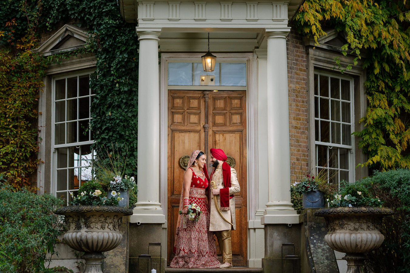 Asian Sikh wedding bride, with a bouquet in her hand and groom holding his kirpan with his left hand on the stairs at Hampton Court House.