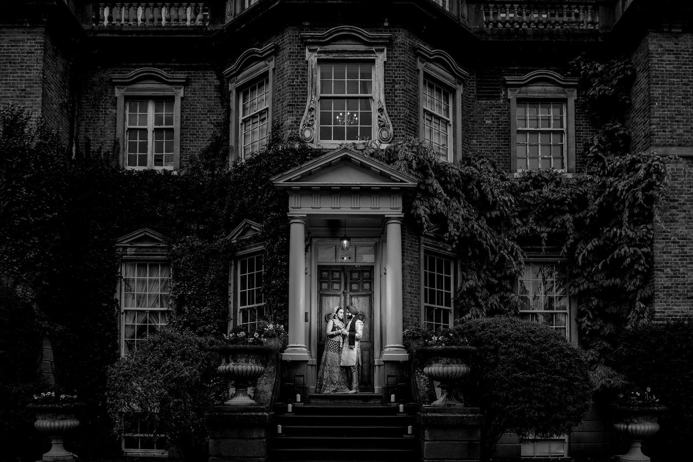 Black and white Asian wedding photography of bride and groom holding hands and looking at each other at Hampton Court House.