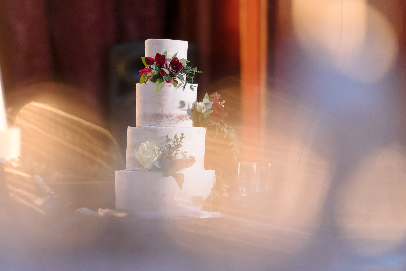 White semi naked wedding cake decorated with red orchids & white roses.