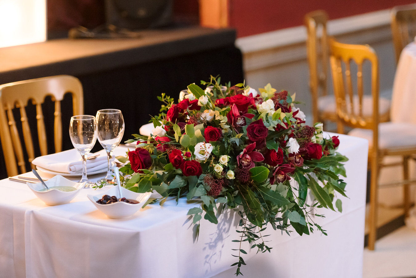 Sweetheart table setting with a winter red and white flower arrangement, a couple of glasses and white napkins