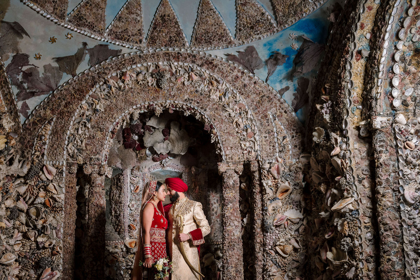 Bride and groom in Sikh Asian wedding standing face to face in the shell grotto at Hampton Court House.